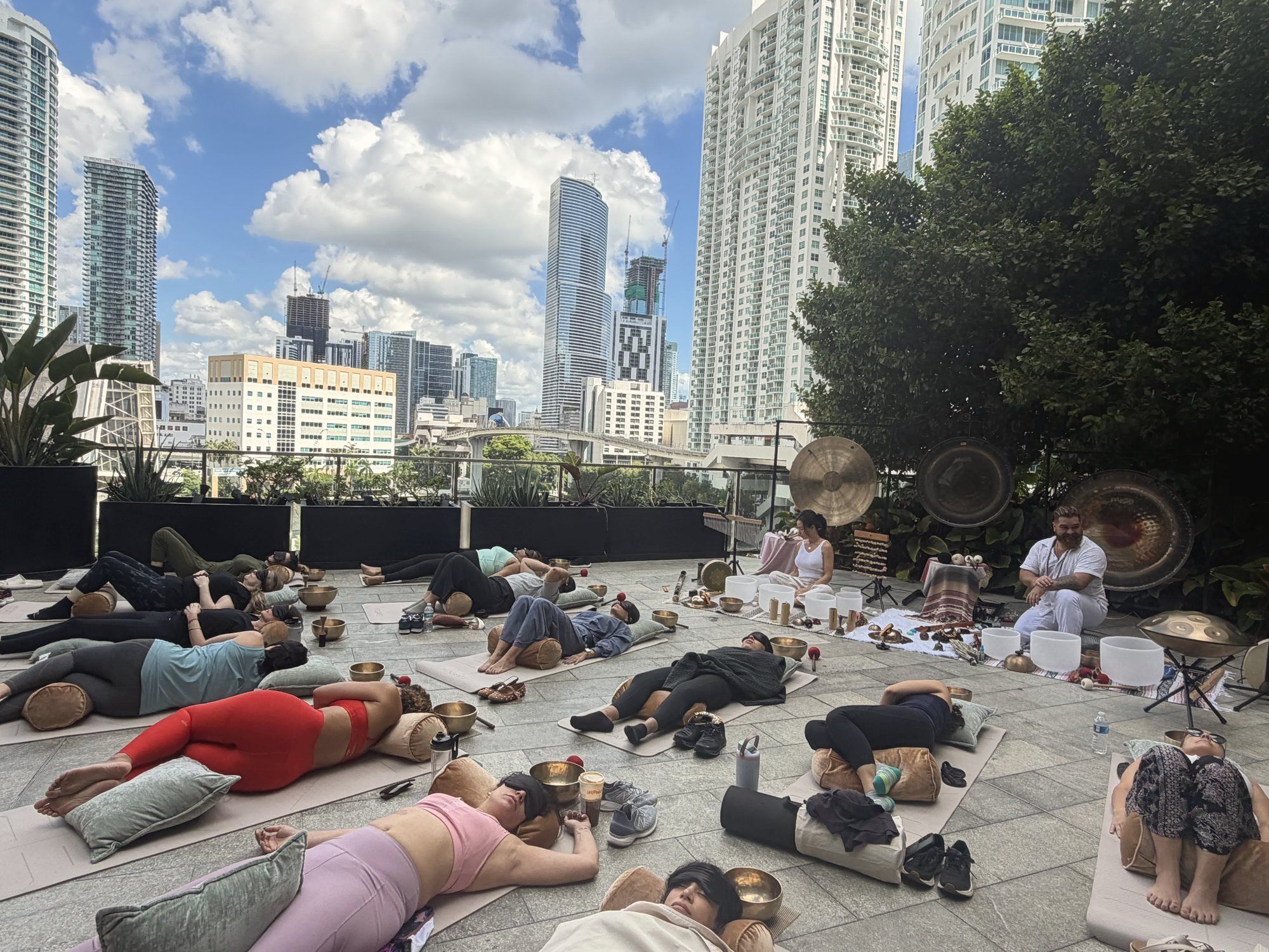 Participants lying on mats across the Puttshack terrace under a blue sky, Juan at the gongs